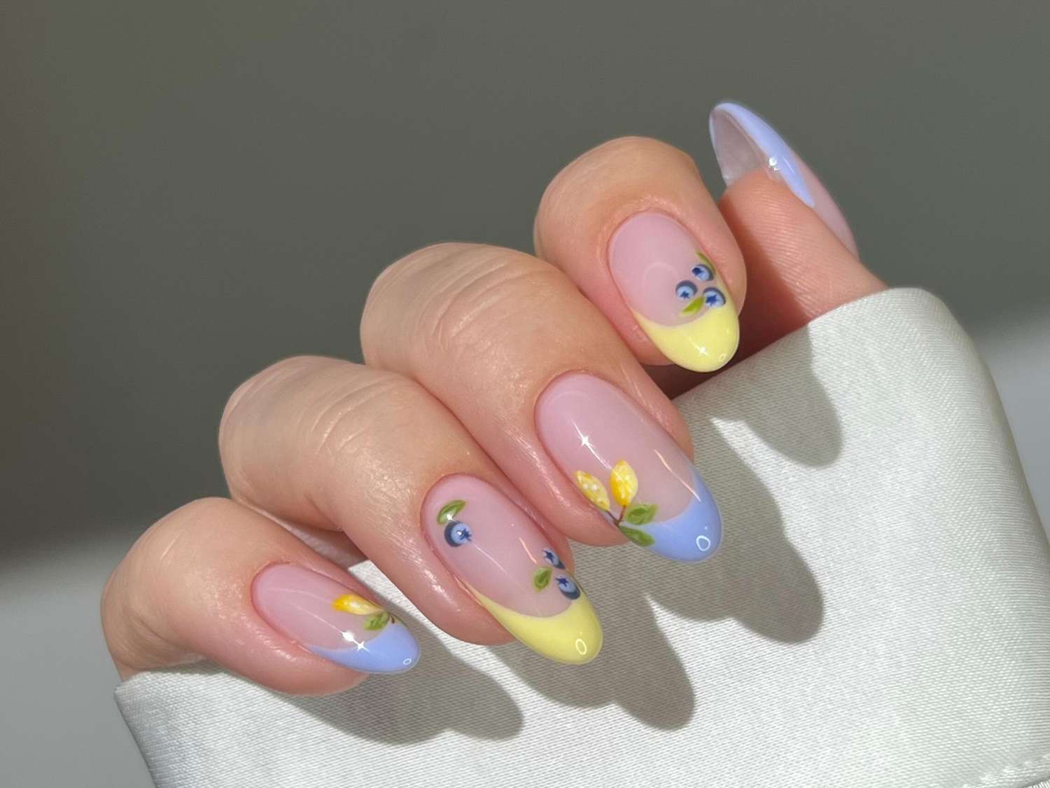 Almond-shaped nails with pastel yellow and blue French tips and delicate floral designs, showcasing a trendy summer 2025 manicure style