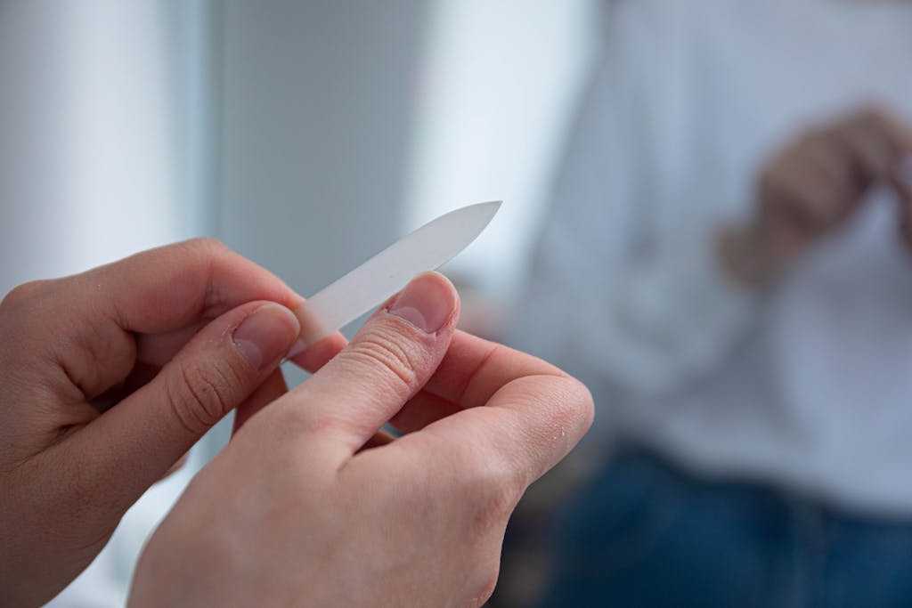 A person uses a glass nail file to groom their nails, reflecting self-care and grooming habits.