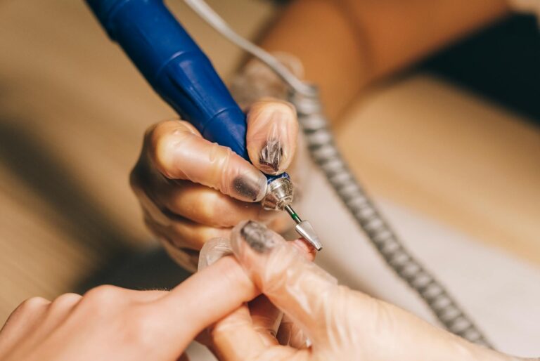 Close-up of a nail technician using an electric file during a manicure session. Ideal for beauty and fashion content.