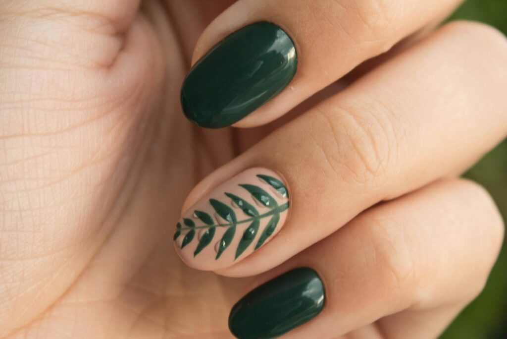 Close-up of a stylish green manicure with a leaf design, showcasing glossy fingernails and natural skin tone.