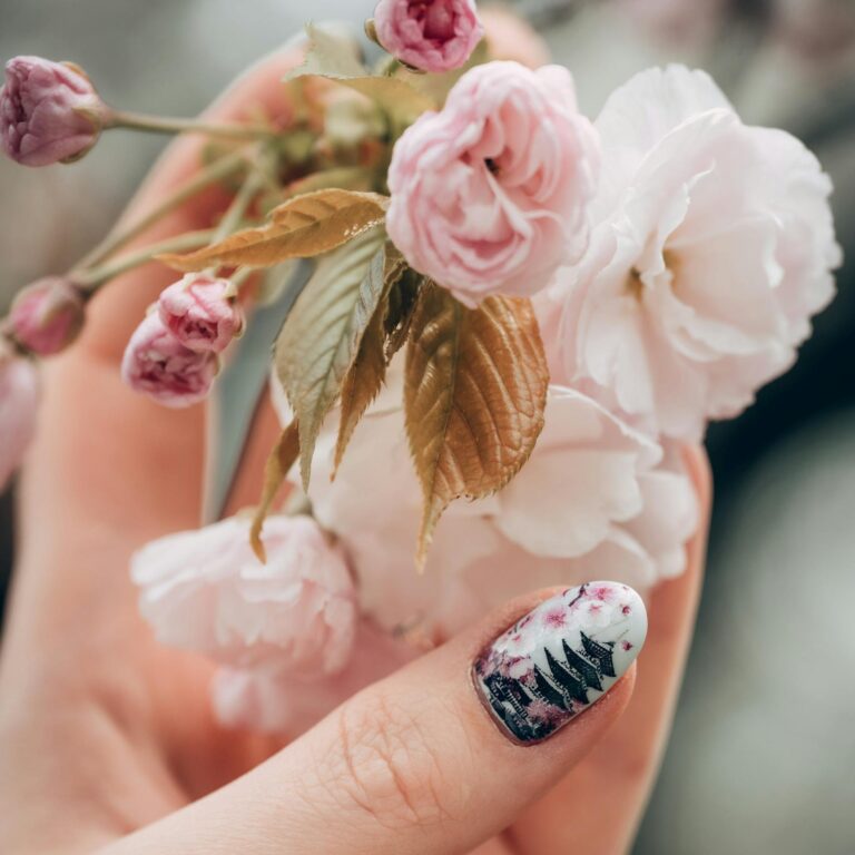Delicate cherry blossoms held by a hand with artistic nails in Tokyo, Japan, showcasing spring beauty.