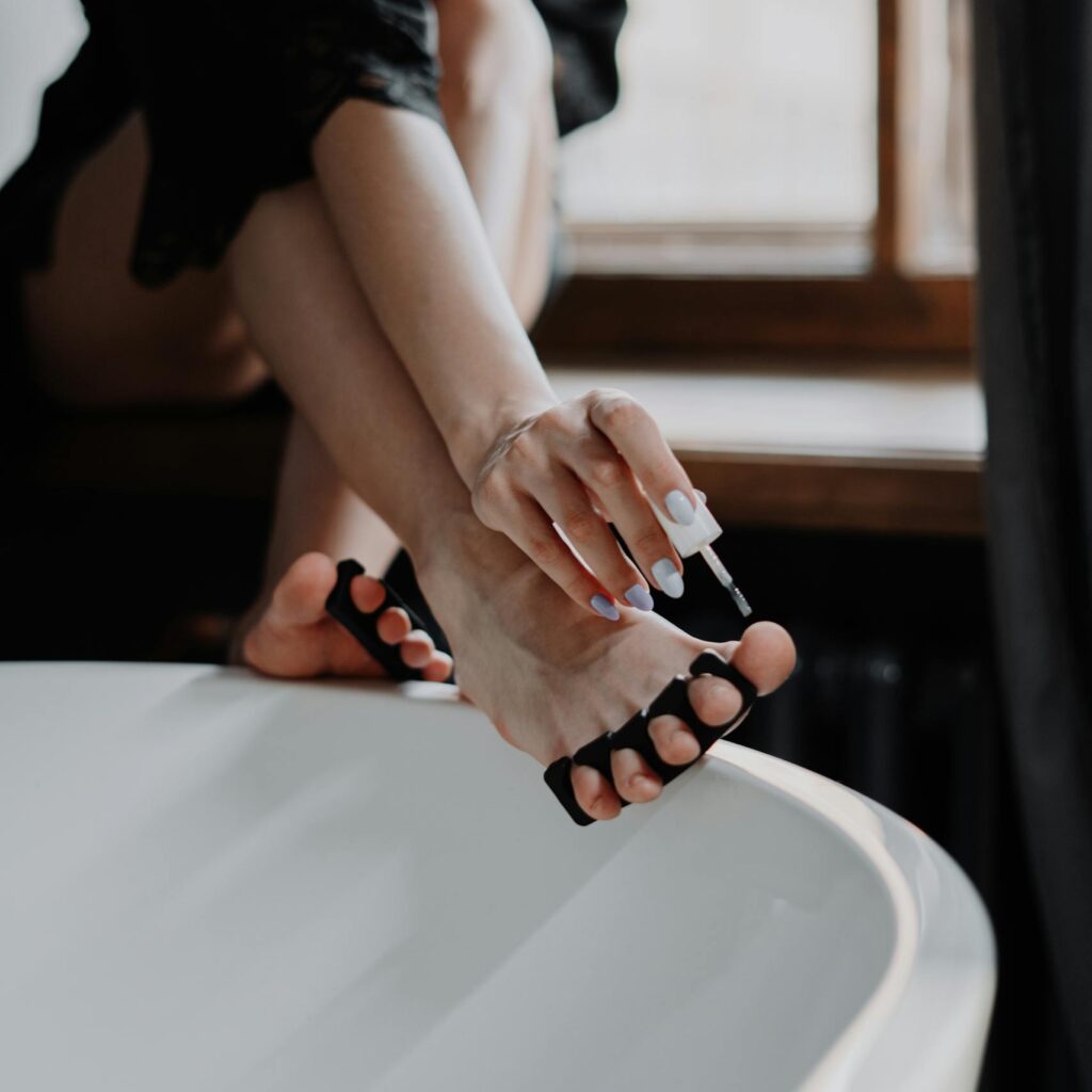 Young woman performing a pedicure by the window, focusing on self-care and beauty.