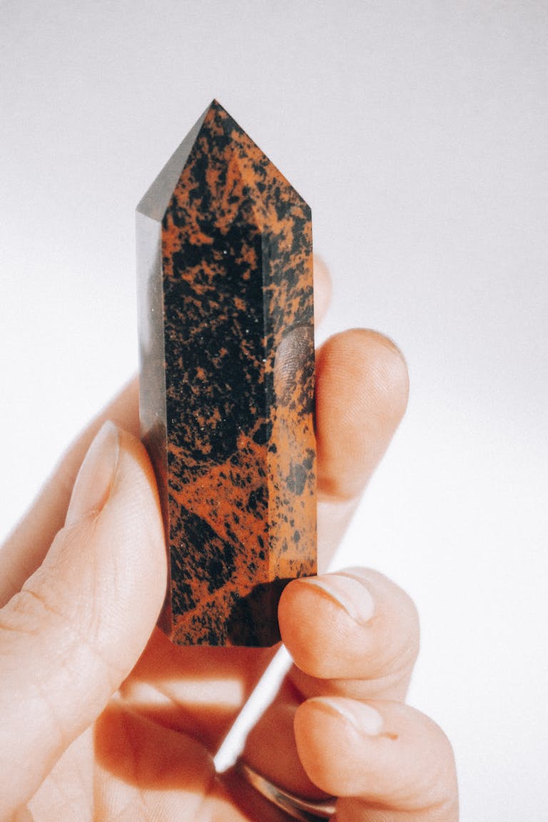 A close-up image showcasing a hand holding a polished obsidian stone against a white background.