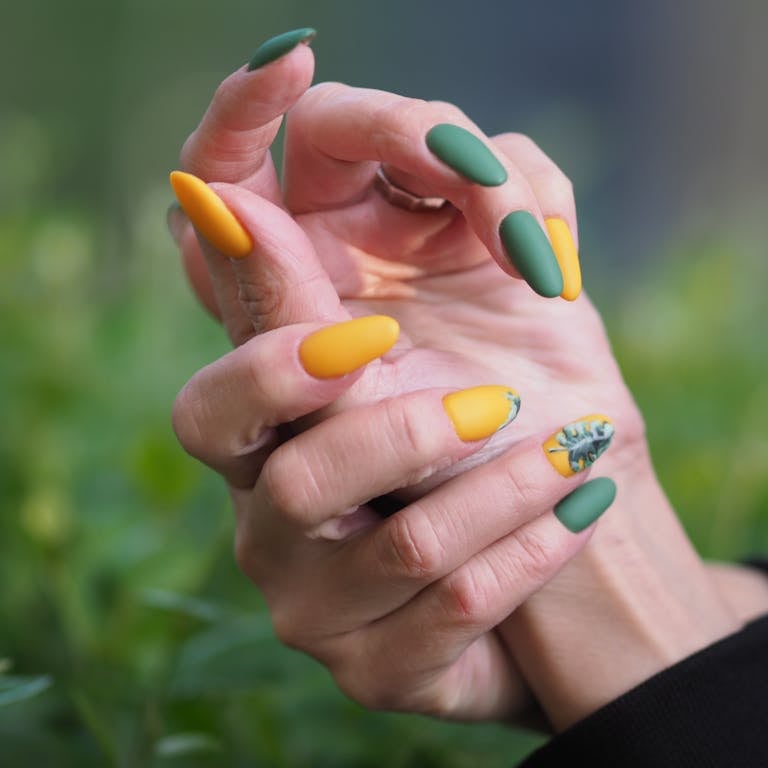 Close-up of hands with green and yellow manicured nails in an artistic pose.