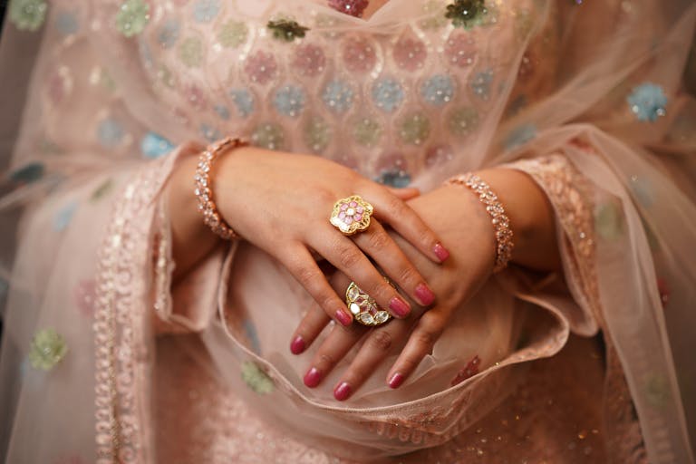 Close-up of a bride's hands adorned with intricate rings and bracelets, wearing a colorful, sparkling dress.