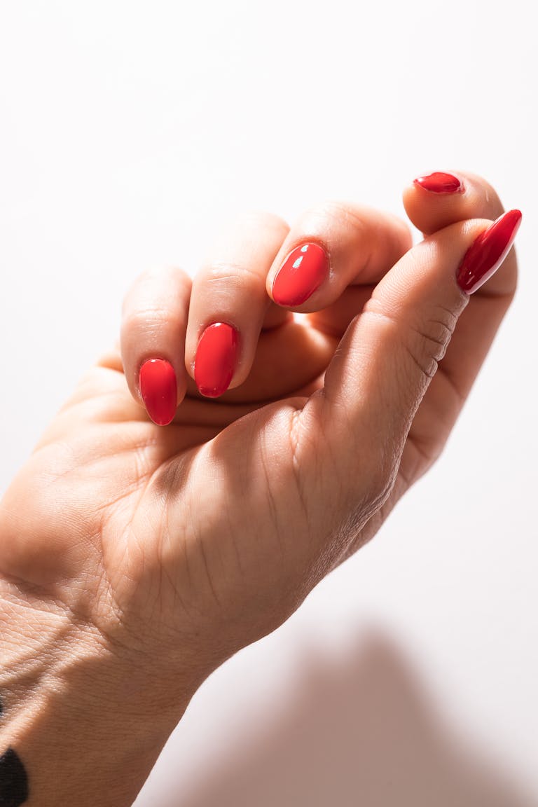 Close-up of a woman's hand with a stylish red manicure, elegantly posed against a light background.