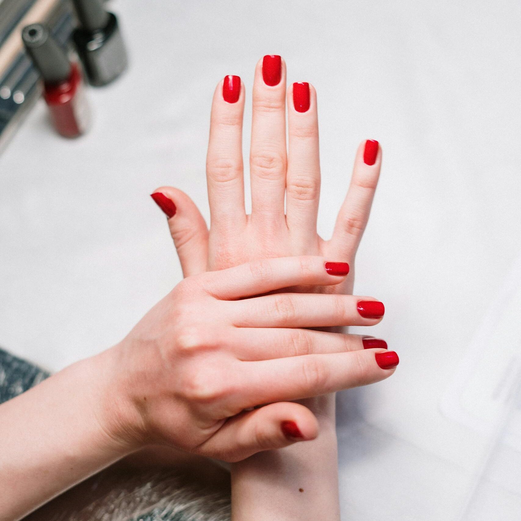 Close-up of elegant red nail polish on hands in a salon setting, showcasing modern manicure art.