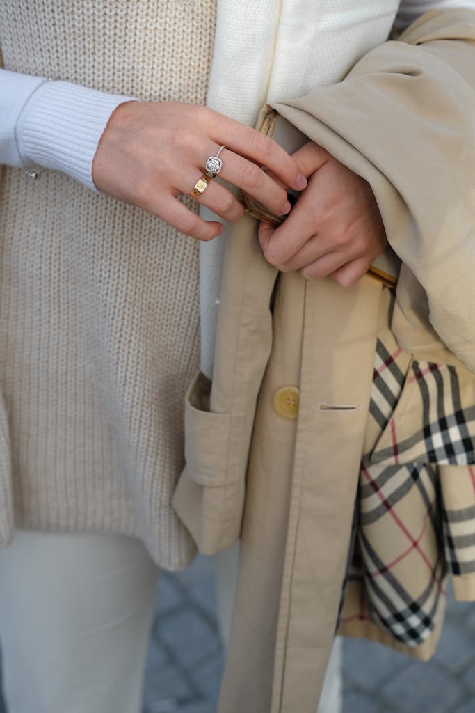 Close-up of a woman's hands featuring elegant rings and a stylish trench coat.