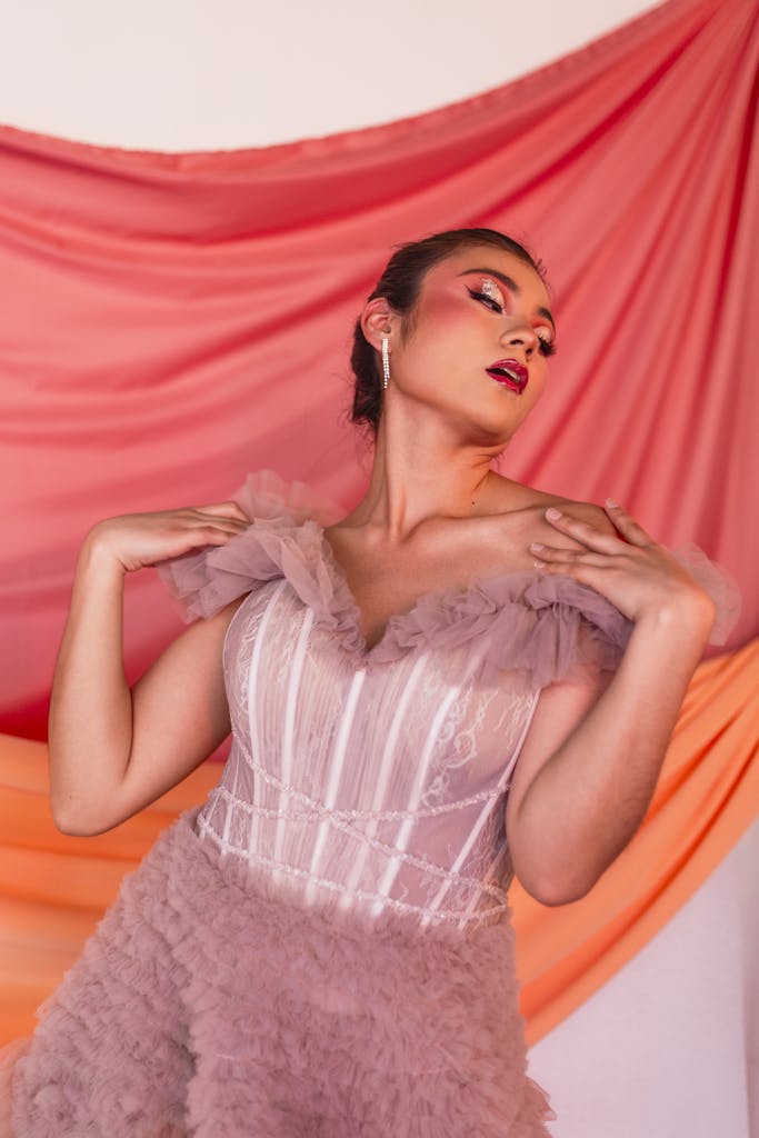 Woman in a glamorous pink ball gown posing against a vibrant backdrop, exuding fashion and elegance.