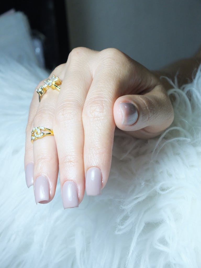 Close-up of a well-manicured hand adorned with gold rings against a soft white background.