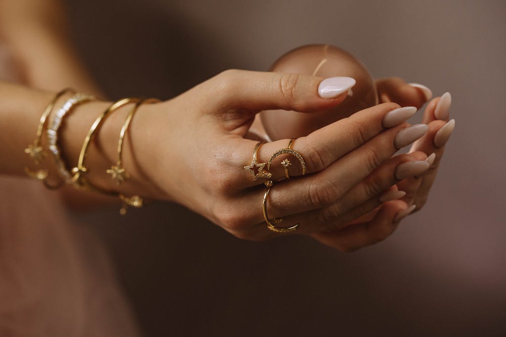 Close-up of hands adorned with gold bracelets and rings holding a delicate object, highlighting elegance and style.