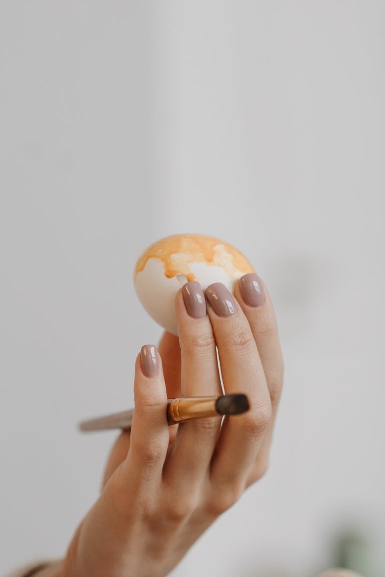 Delicate hand painting an Easter egg with a brush in a soft vertical shot.
