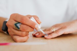 Nakładanie bezbarwnego preparatu pędzelkiem na naturalne paznokcie podczas manicure