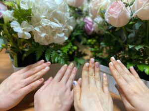 Cztery dłonie z delikatnym manicure na tle bukietu białych hortensji i różowych róż