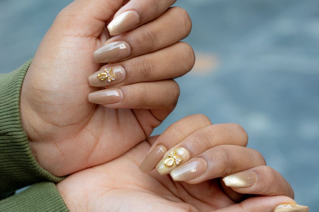 Dłonie z beżowym manicure i złotymi ozdobami 3D na wybranych paznokciach