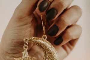 Dłoń z manicure trzymająca złoty, brokatowy sierp księżyca z gwiazdą – inspiracja na paznokcie na Andrzejki