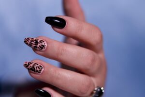 Zbliżenie dłoni z manicure w panterkę: paznokcie w beżowo-brązowe cętki z czarnymi obrysami obok paznokci w czarnym kolorze