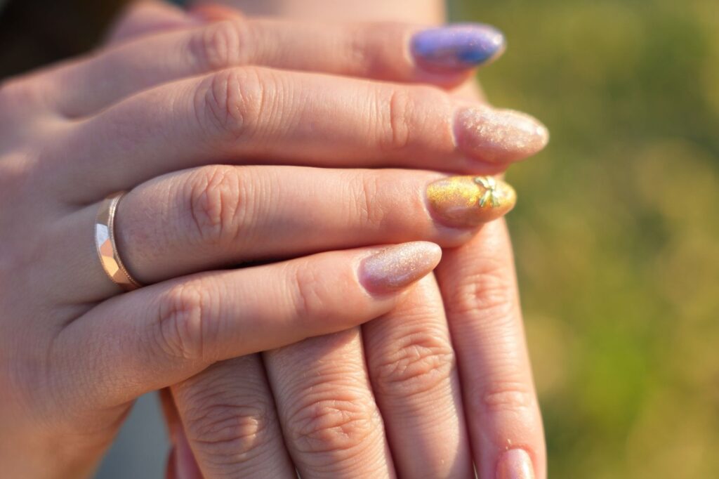 Dłonie z opalizującym lawendowym manicure i paznokciami nude z brokatem oraz złotymi kokardkami