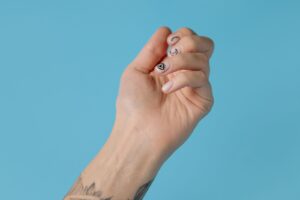 Dłoń z nude manicure, na trzech paznokciach cienkie czarne wzory oczu i półksiężyca w stylu stempla, niebieskie tło