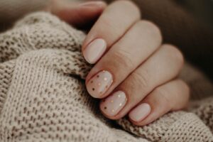 Dłoń z nude manicure w złote kropki na beżowym, grubym swetrze z dzianiny